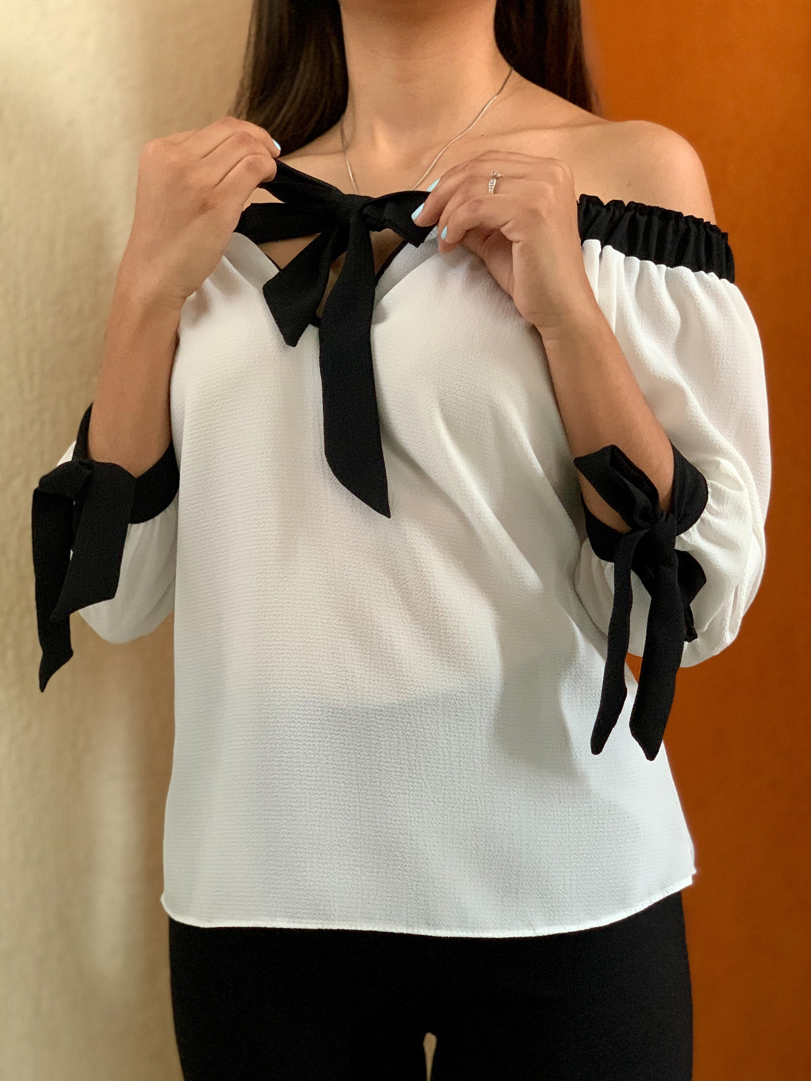 Blusa campesina blanca con corbatín negro y cintas en las muñecas.