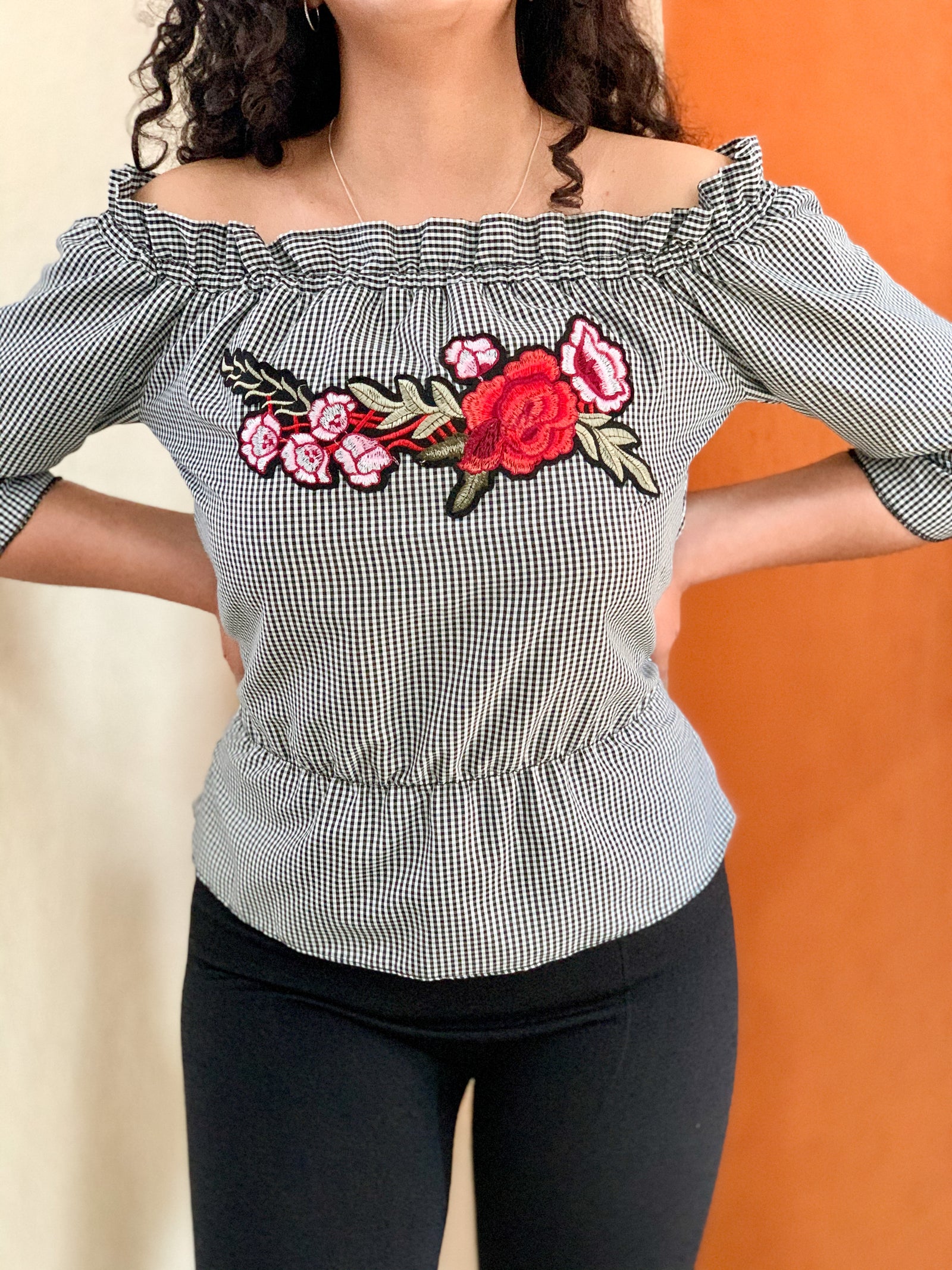 Blusa campesina en tela de cuadros con bordado de flor.